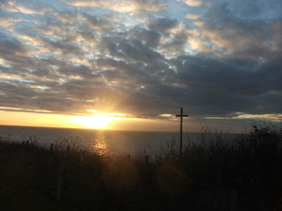 sunset over the sea behind a cross.